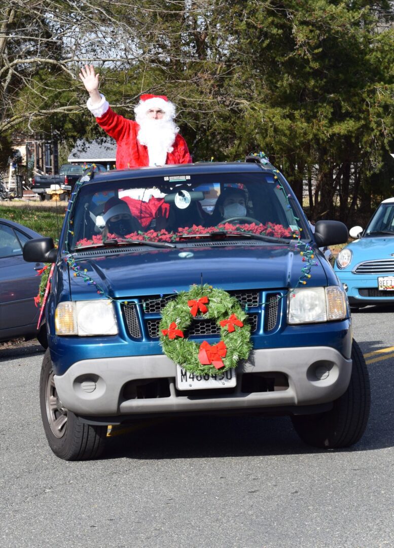 A man in santa claus costume waving from the back of his truck.