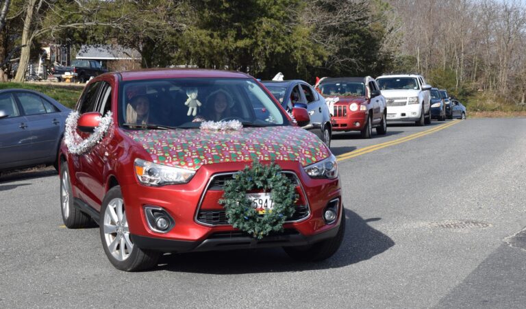 A red car with christmas wrapping on the hood.