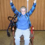 A woman sitting in a rocking chair with her arms raised.