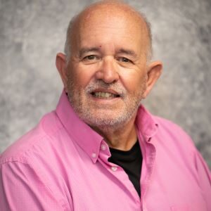 A man in a pink shirt is smiling for the camera.