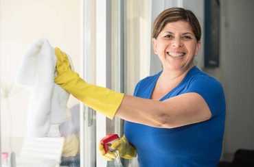 A woman in blue shirt and yellow gloves cleaning window.